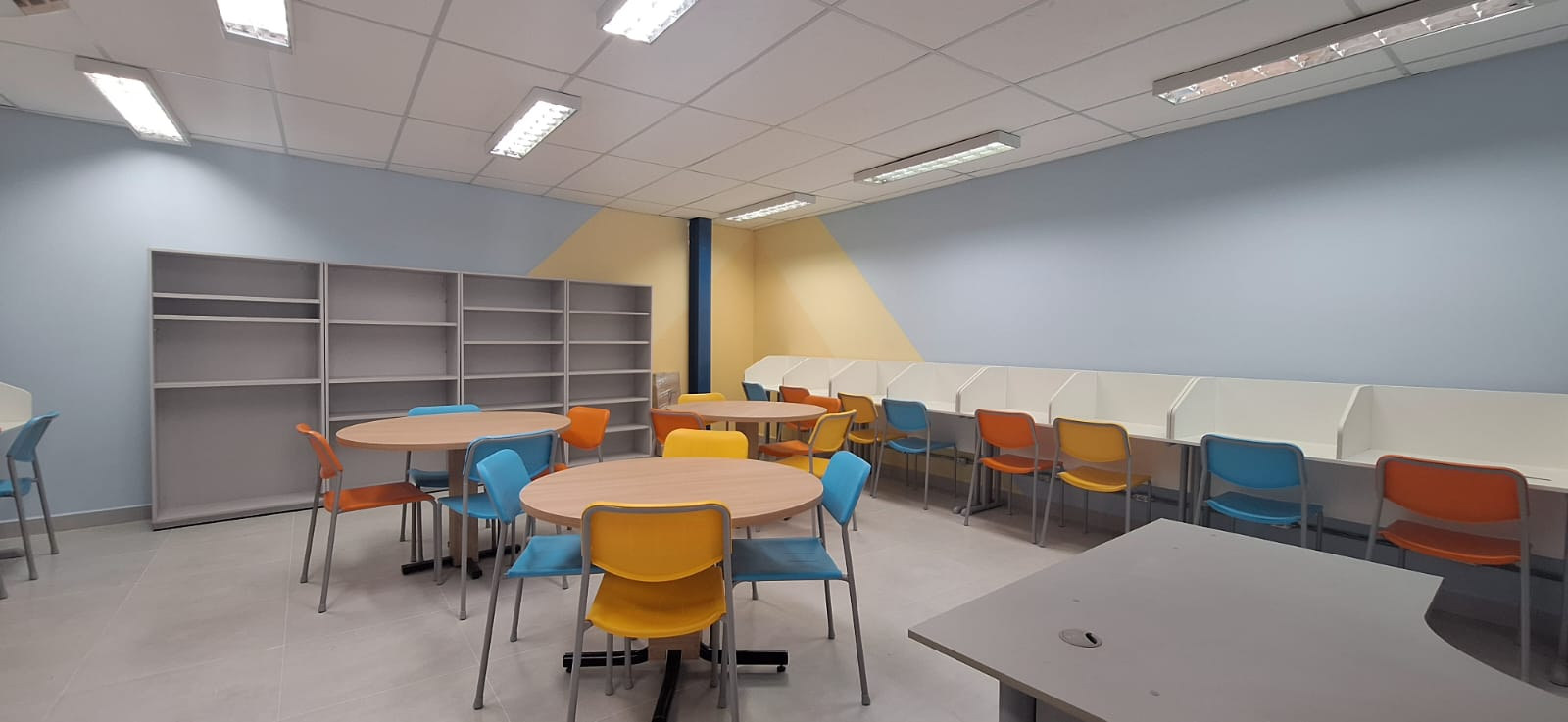 Biblioteca e área de convivência do Colégio Anglo, com mesas, cadeiras e estantes.