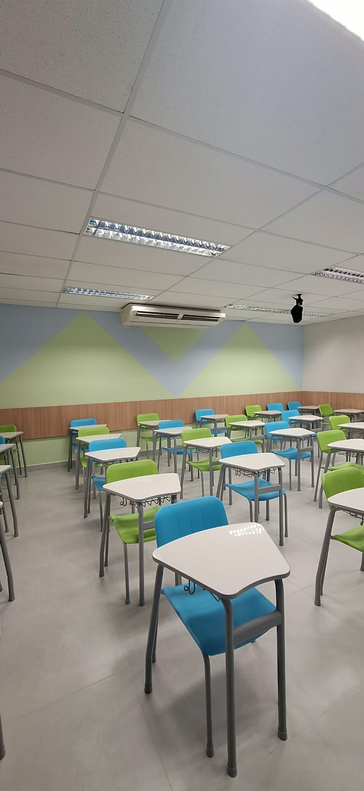 Área de leitura e aprendizagem do Colégio Anglo com mesas, cadeiras e estantes.