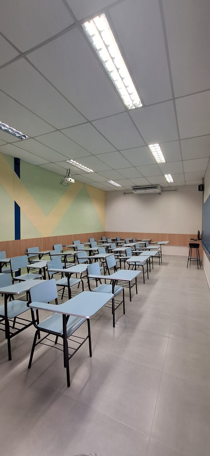 Sala de aula do Colégio Anglo com carteiras, iluminação e parede geométrica em tons suaves.